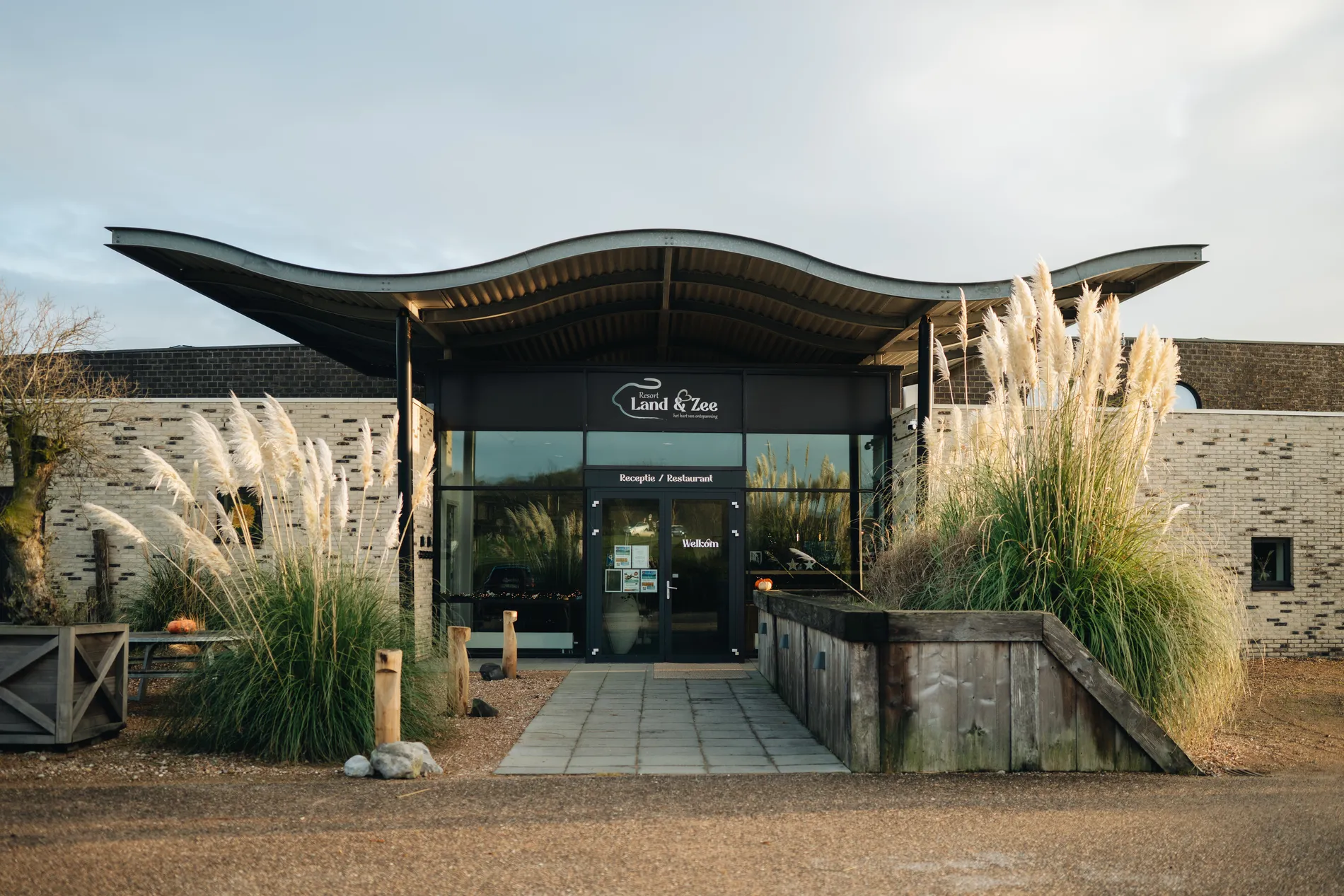 De moderne, architectonische entree van Restaurant Zeeuws Verlangen en Resort Land & Zee, omgeven door wuivend pampasgras.