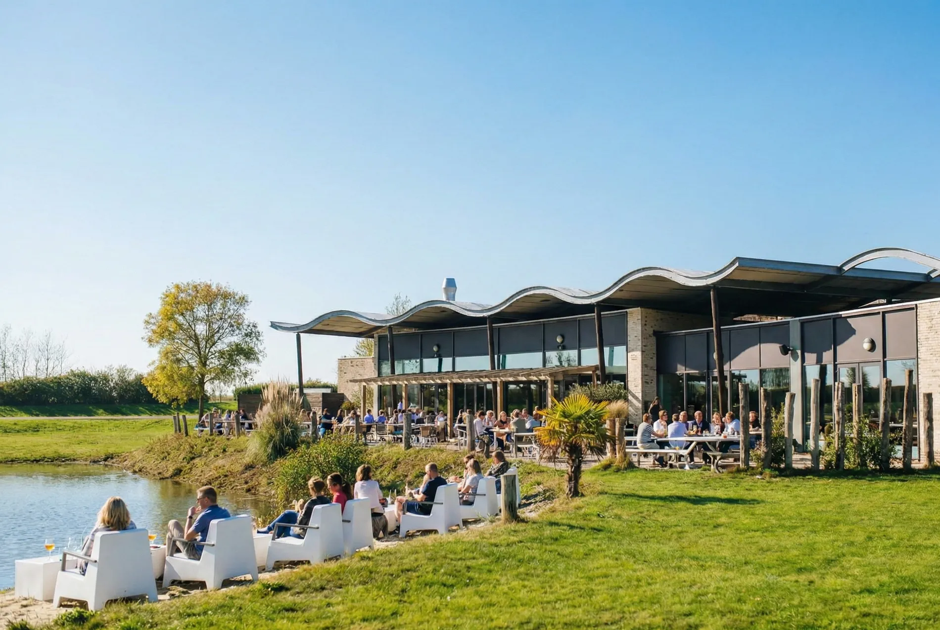 Panoramisch uitzicht op het zonnige terras van Restaurant Zeeuws Verlangen met gasten in witte loungezetels aan het water onder een iconisch golvend dak.